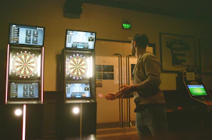People intensely focused on their dart throws, with sports events visible on the large TV screens behind them.