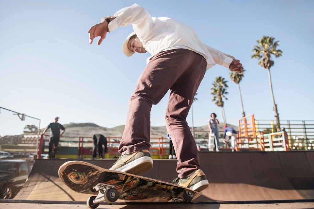 man in white dress shirt and brown pants riding skateboard during daytime