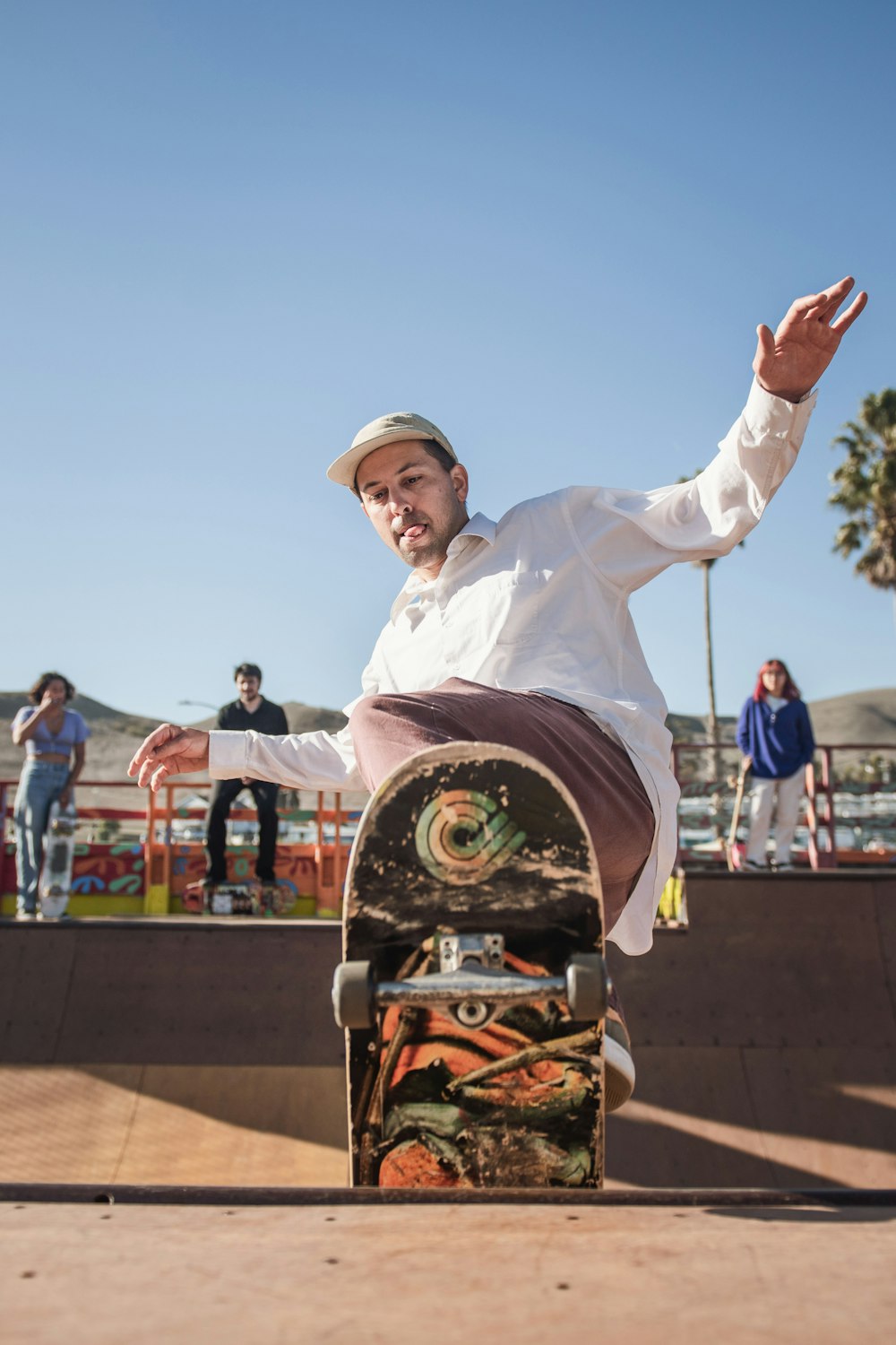 man in white dress shirt and brown hat holding black skateboard