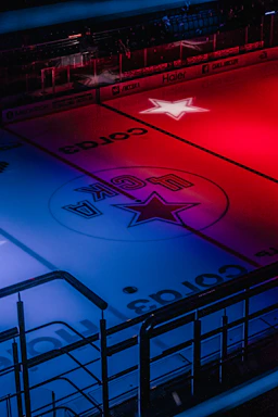 A sleek ice hockey arena bathed in deep navy blue lighting, with a player poised mid-stride on the ice.