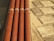 Four horizontal orange pipes are held in place by metal brackets. To the right, a surface comprising square stone tiles arranged in a geometric pattern is visible. The lighting creates warm highlights on the pipes and a textured effect on the tiles.