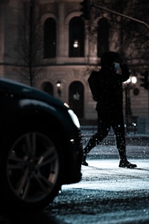 Close-up of a masked figure lurking near a parked car at night.