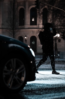 Close-up of a masked figure lurking near a parked car at night.