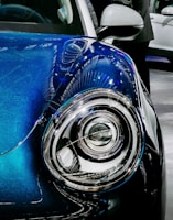 Close-up of a car’s headlight and grille with dark blue accents in a minimalist setting.