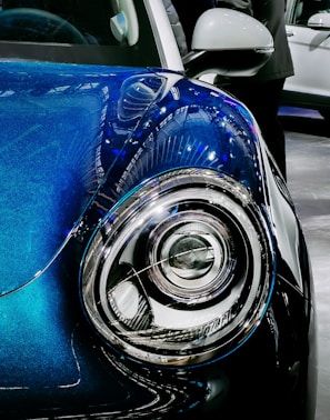 Close-up of a car’s headlight and grille with dark blue accents in a minimalist setting.