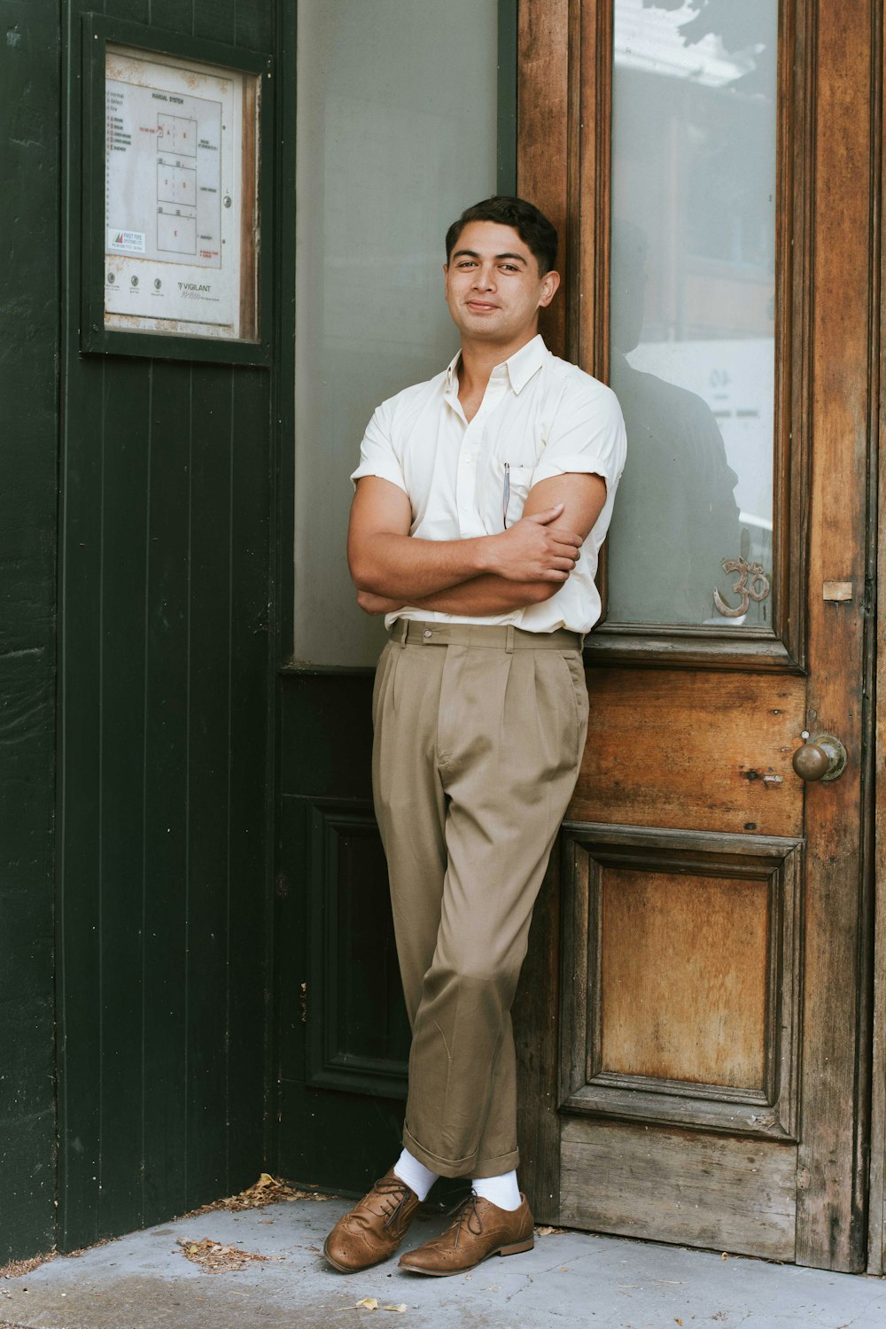 man in white button up shirt and brown pants standing beside brown wooden door