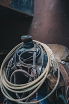 A close-up view of a weathered leather saddle with intertwined ropes and leather straps, creating a rustic and vintage ambiance. The texture of the leather is prominent, highlighting its well-used state.