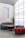 A modern interior space featuring stylish, minimalist furniture including a curved gray sofa, a cylindrical red pouf, and a teal pouf. A round wooden coffee table sits in the center. A large frosted glass wall allows diffused light to fill the room, creating a calm and serene ambiance. A tall green cactus in a pot adds a natural element to the setting.