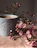 A hand holding a sublimation mug with a soft pink and earthy boho design, surrounded by dried flowers.