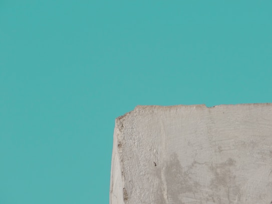 A textured, roughly cut piece of concrete or stone appears in the lower part of the image against a solid teal background.