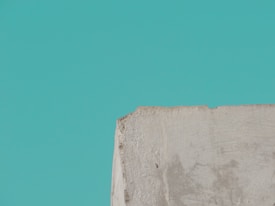A textured, roughly cut piece of concrete or stone appears in the lower part of the image against a solid teal background.