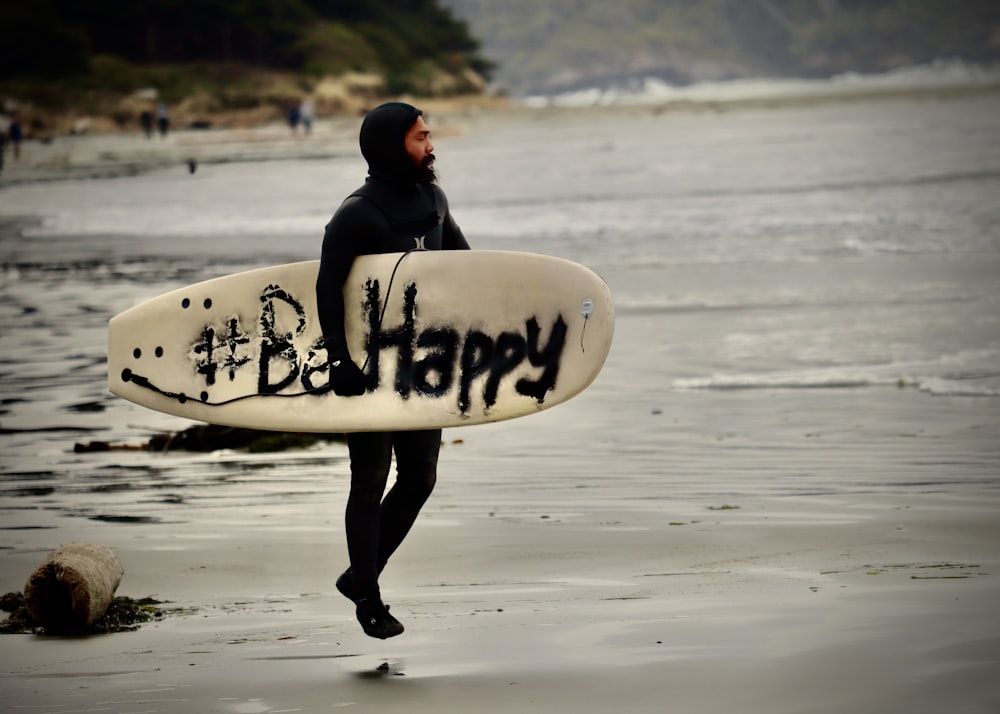 man in black hoodie carrying white surfboard walking on beach during daytime