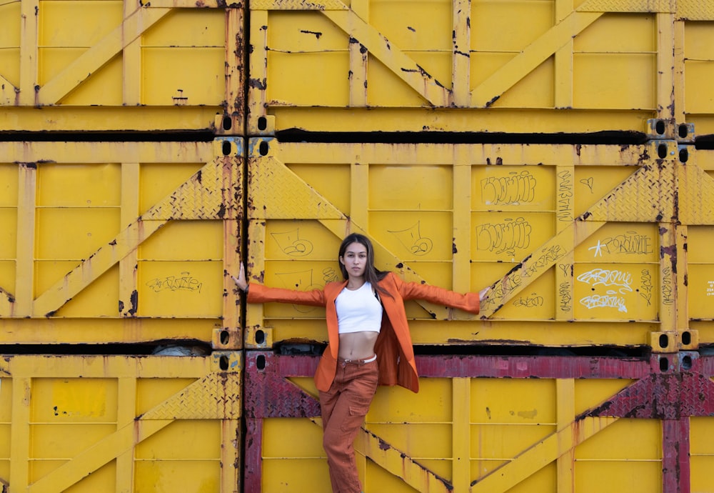 woman in white long sleeve shirt and brown pants standing beside yellow metal wall