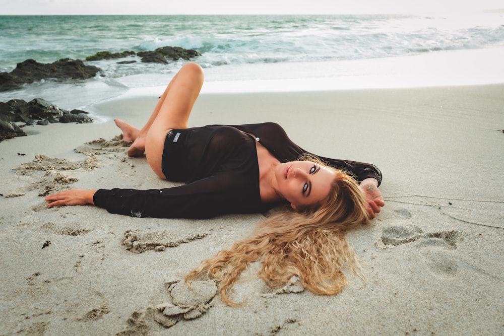 woman in black tank top and black shorts lying on beach sand during daytime