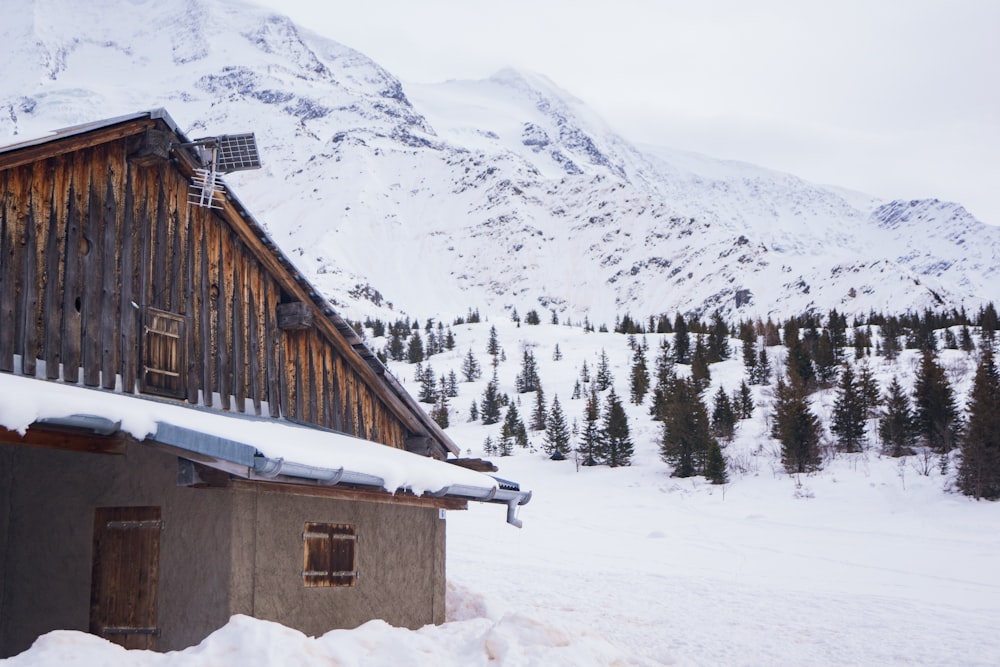 casa de madeira marrom no chão coberto de neve perto da montanha coberta de neve durante o dia