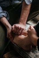 Two hands are gently massaging a foot, suggesting a moment of relaxation or care. The person receiving the massage is wearing dark pants and a light shirt.