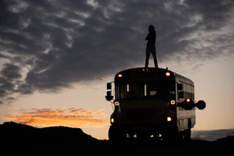 man in black jacket standing on top of yellow bus during sunset