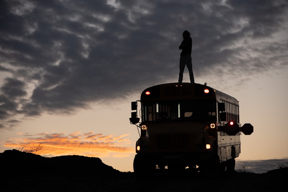 man in black jacket standing on top of yellow bus during sunset