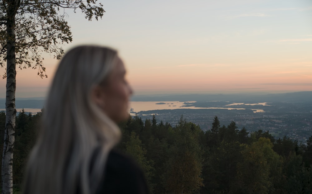 woman in black jacket standing near green trees during daytime