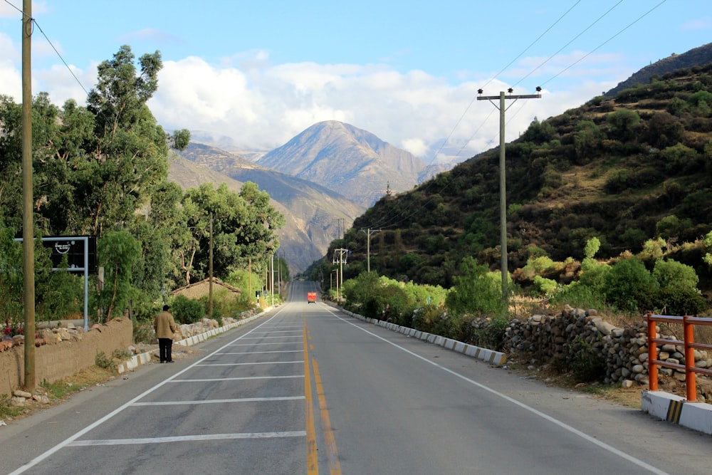 gray concrete road between green trees and mountains during daytime