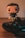 A pop culture figurine with a stylized design stands next to a video game controller on a wooden surface. The figurine has a cute, cartoonish appearance with an oversized head and minimal facial features. The game controller is a modern design with colorful buttons and analog sticks.