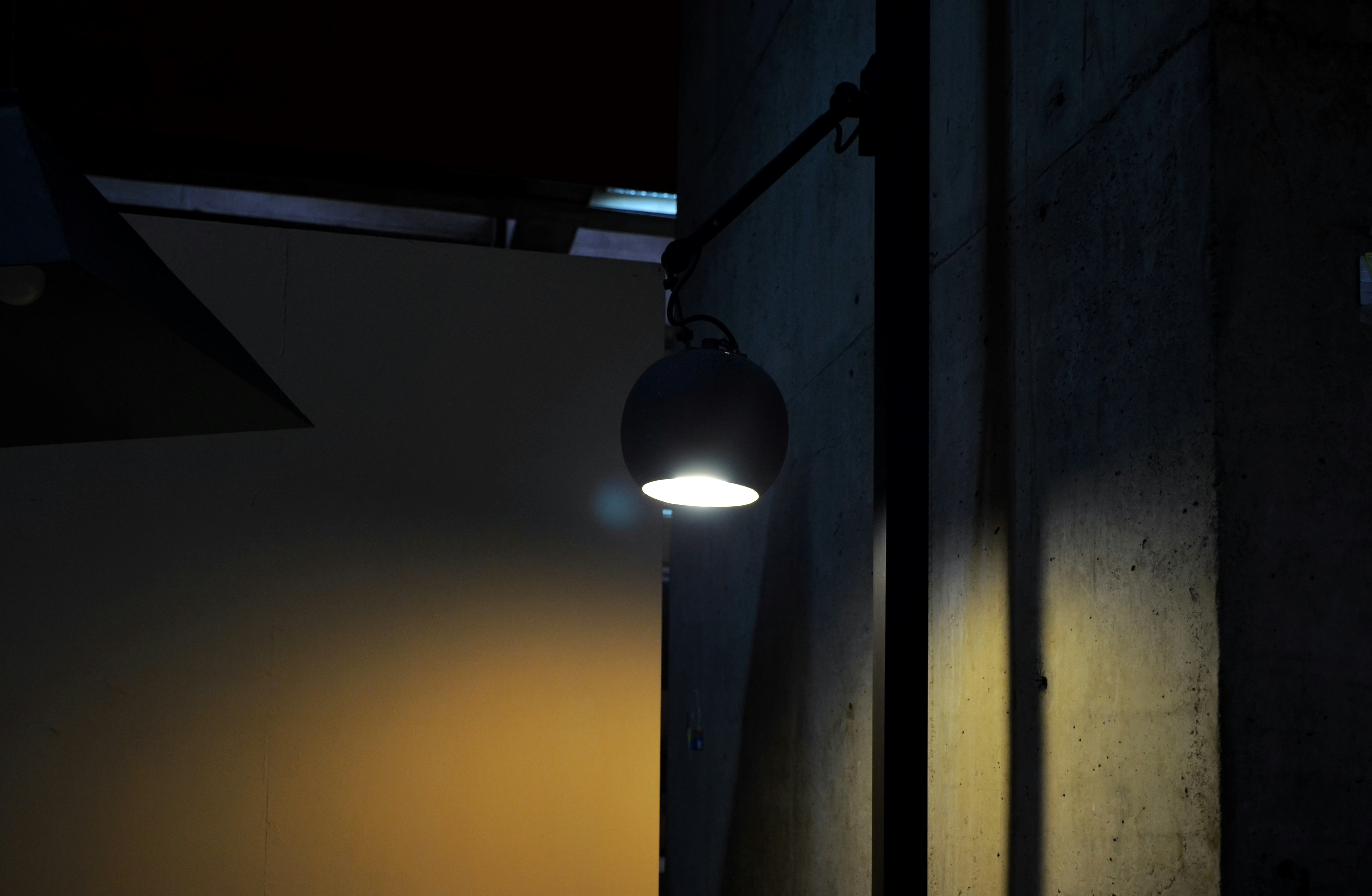 Sleek articulated desk lamp in matte black with warm LED light illuminating an architect's drawing board in a minimal studio with exposed concrete walls