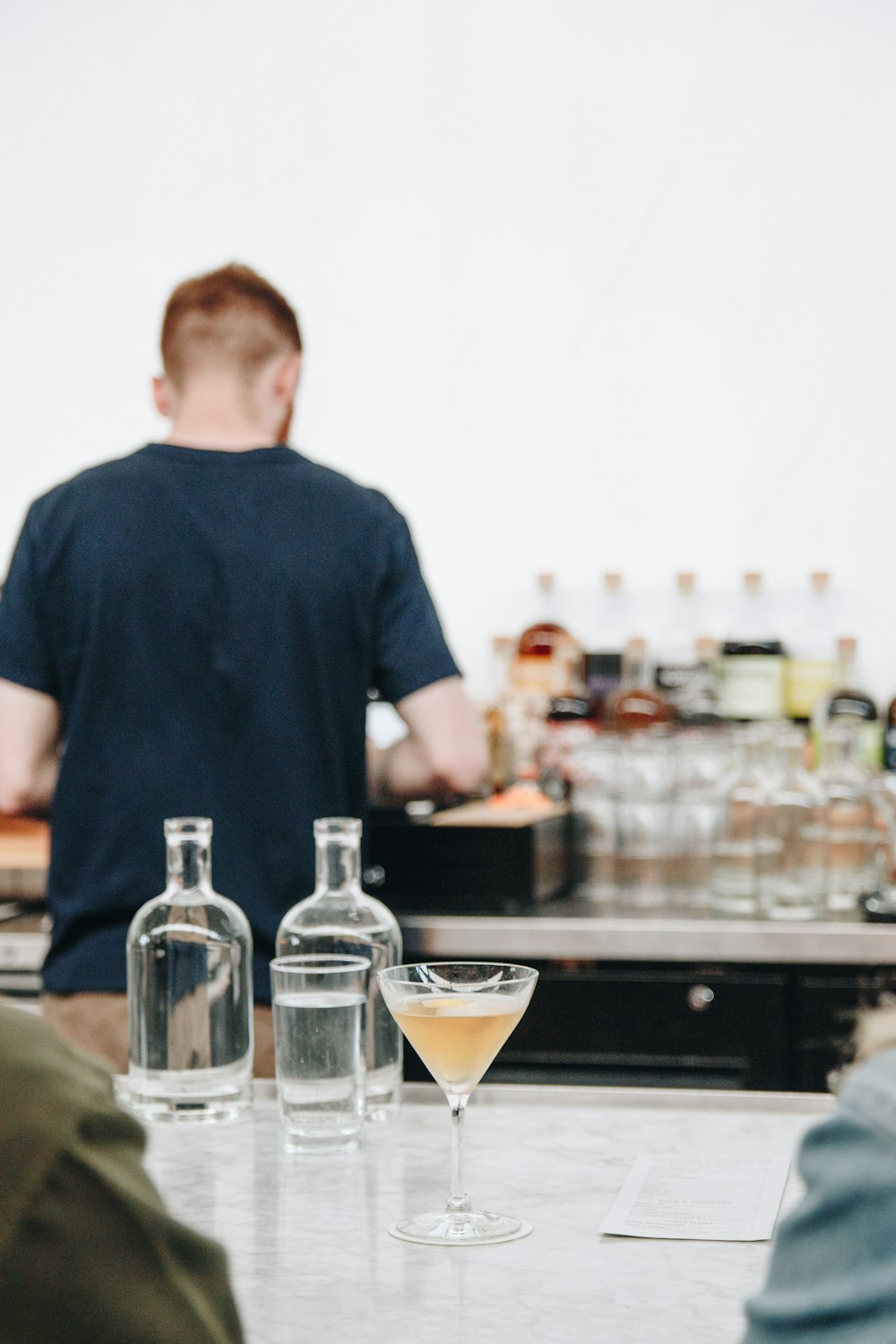 man in black crew neck t-shirt standing in front of table with clear glass bottles