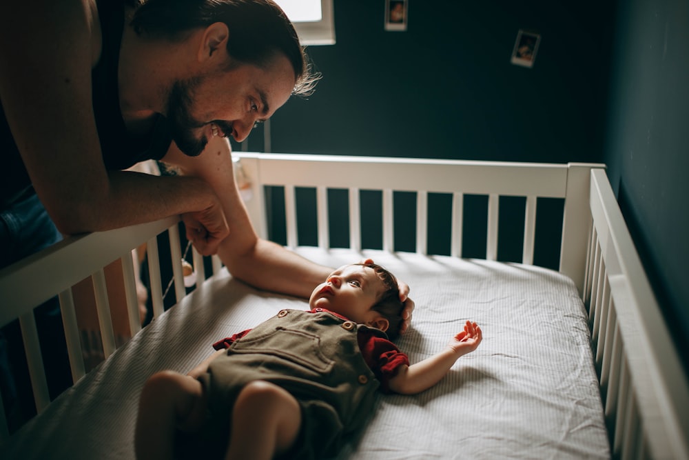 man in green shirt lying on bed beside baby in red shirt