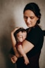 A woman gently cradles a sleeping baby in her arms, both appearing peaceful. The setting has a soft, muted color palette, adding warmth to the intimate scene. The woman’s serene expression and careful hold suggest tenderness and protection.