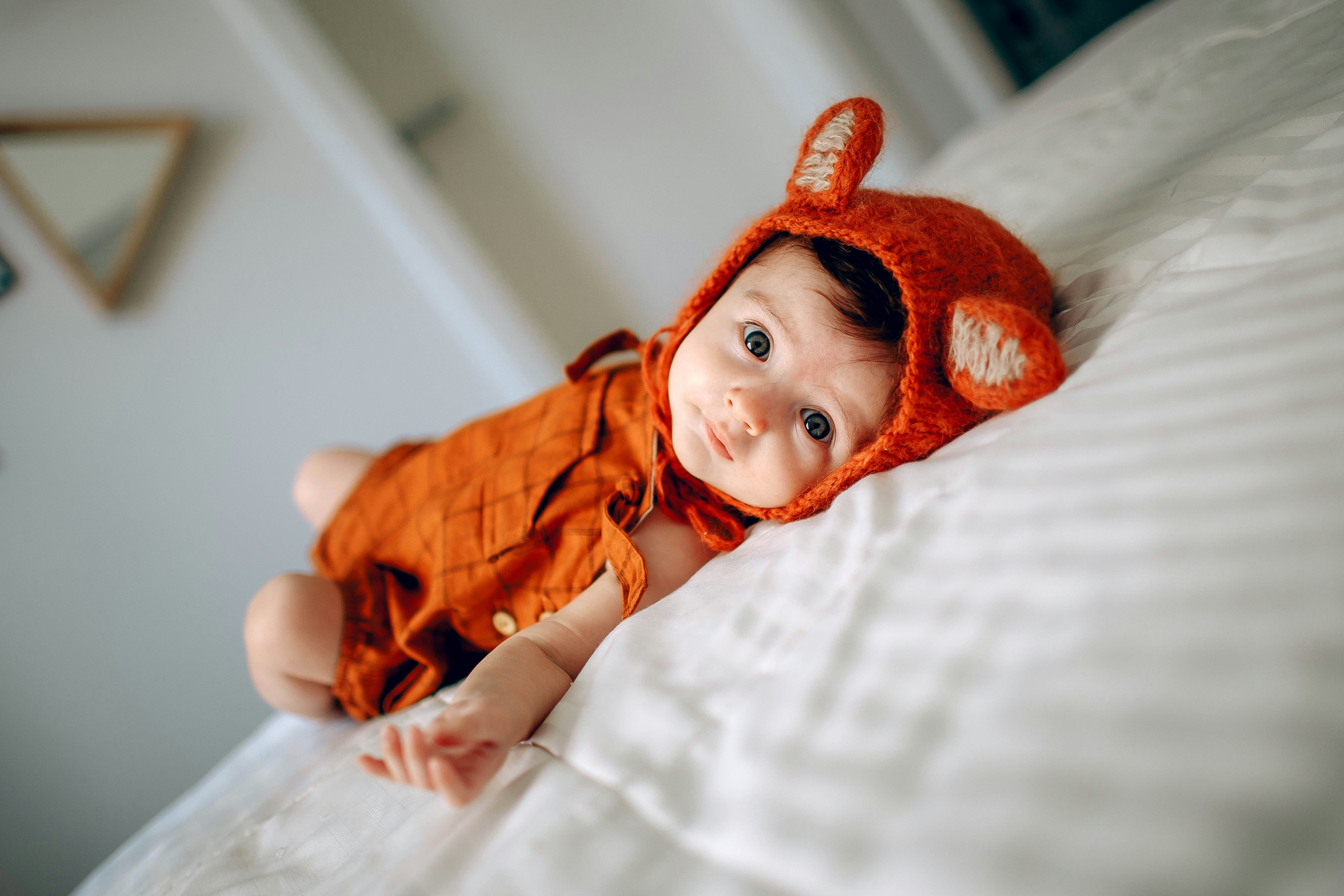 baby in orange dress lying on white bed