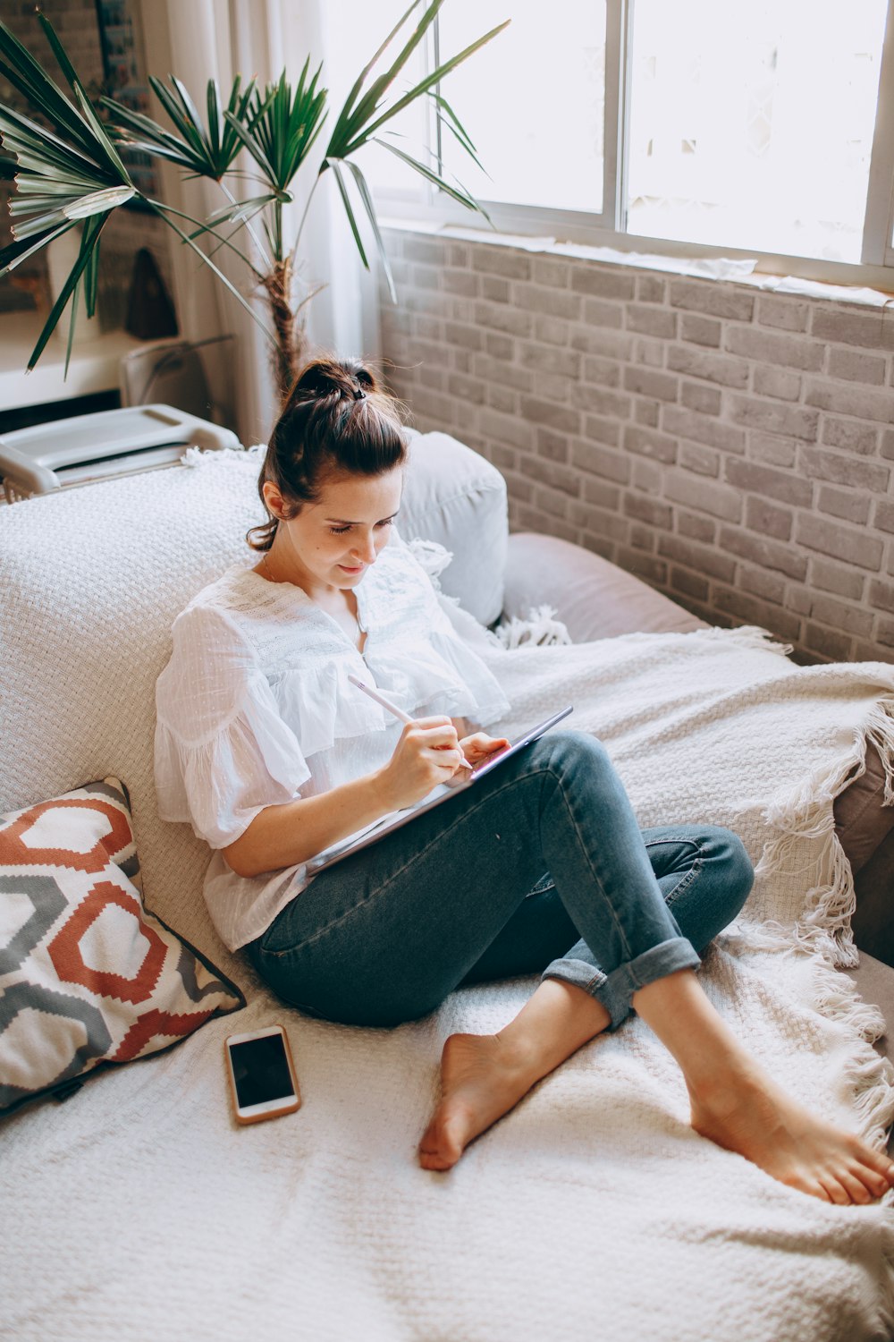 woman in white shirt and blue denim jeans sitting on white and brown couch
