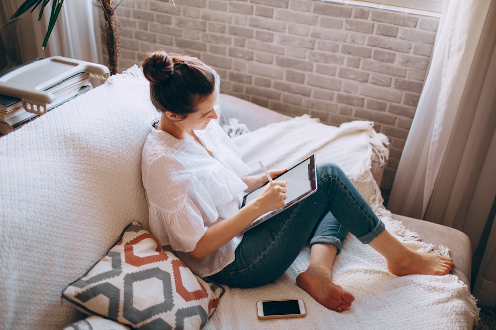 woman in white shirt and blue denim jeans sitting on white couch