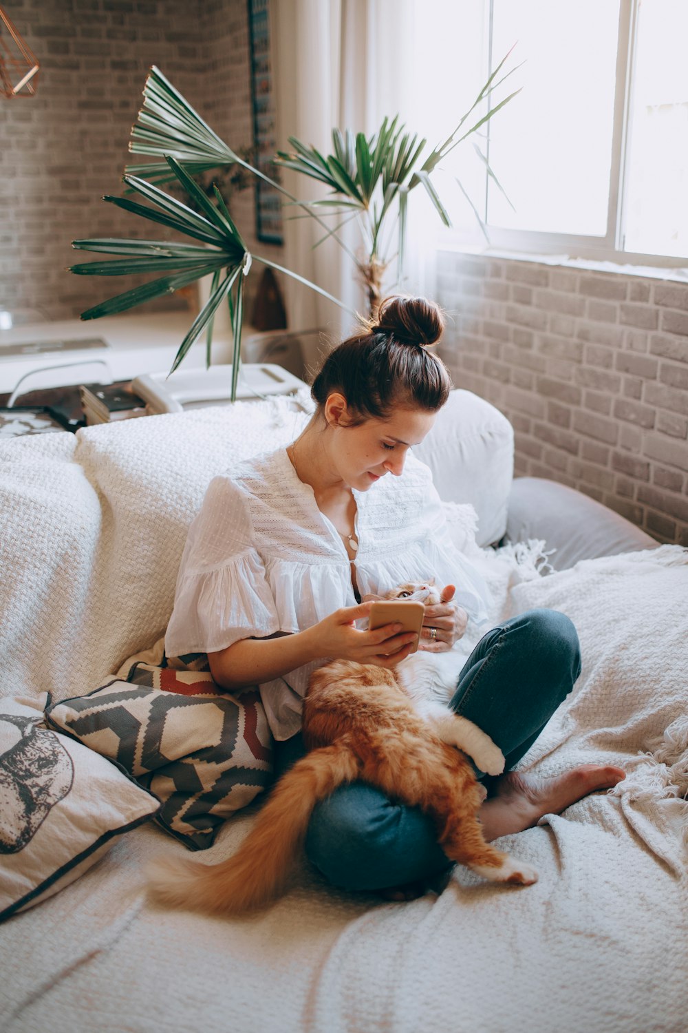 woman in white long sleeve shirt sitting on bed beside brown dog