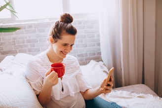 A friendly woman smiling while holding a smartphone in a cozy home environment.