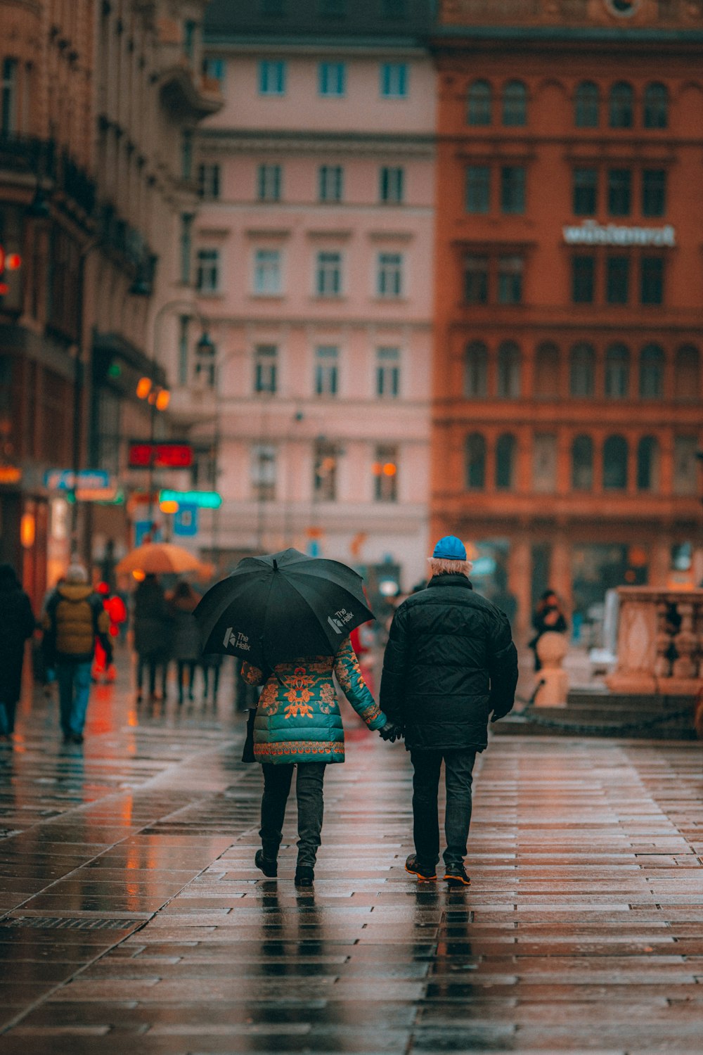 personne en veste noire tenant un parapluie marchant sur le trottoir pendant la journée