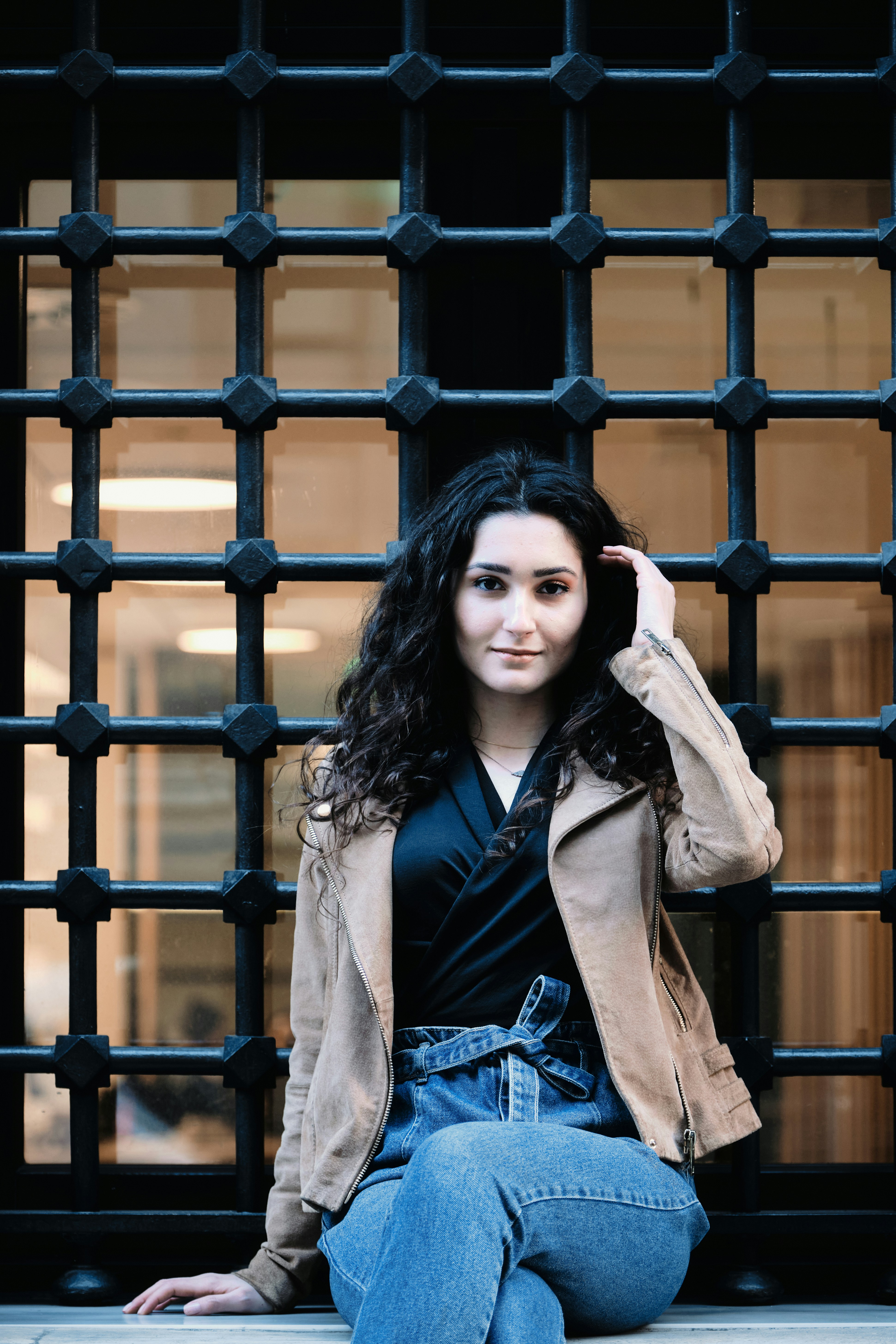 갈색 금속 울타리 옆에 서 있는 갈색 코트를 입은 여자