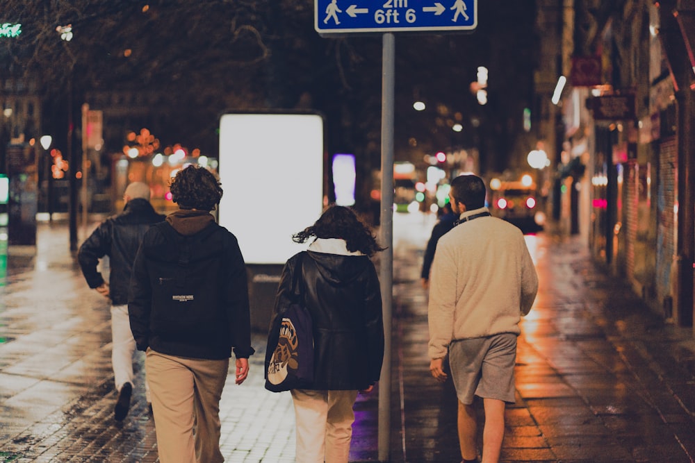 man in black jacket and brown pants walking on sidewalk during night time