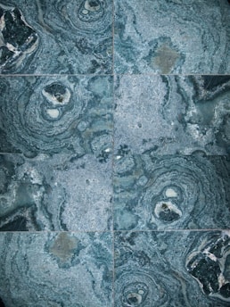 The image features a detailed close-up view of marble or stone tiles with intricate swirling patterns in shades of blue and gray. The tiles are arranged in a symmetrical pattern, creating a visually pleasing and consistent design.