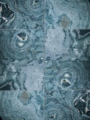 The image features a detailed close-up view of marble or stone tiles with intricate swirling patterns in shades of blue and gray. The tiles are arranged in a symmetrical pattern, creating a visually pleasing and consistent design.