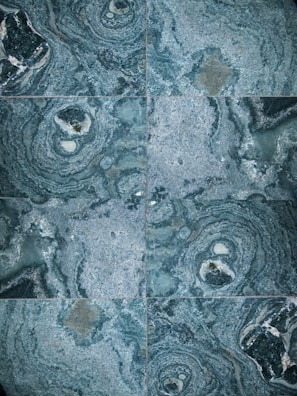 The image features a detailed close-up view of marble or stone tiles with intricate swirling patterns in shades of blue and gray. The tiles are arranged in a symmetrical pattern, creating a visually pleasing and consistent design.