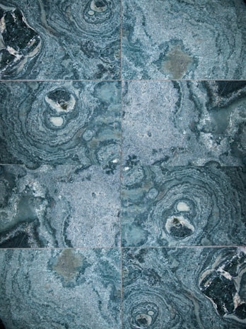 The image features a detailed close-up view of marble or stone tiles with intricate swirling patterns in shades of blue and gray. The tiles are arranged in a symmetrical pattern, creating a visually pleasing and consistent design.