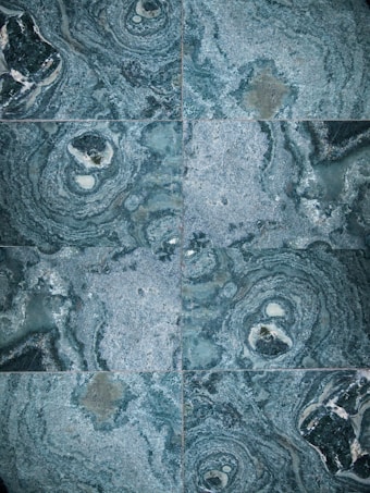 The image features a detailed close-up view of marble or stone tiles with intricate swirling patterns in shades of blue and gray. The tiles are arranged in a symmetrical pattern, creating a visually pleasing and consistent design.