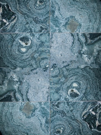 The image features a detailed close-up view of marble or stone tiles with intricate swirling patterns in shades of blue and gray. The tiles are arranged in a symmetrical pattern, creating a visually pleasing and consistent design.