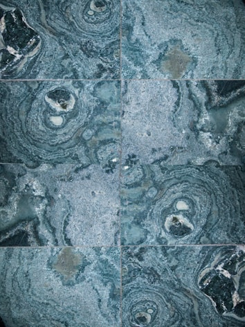 The image features a detailed close-up view of marble or stone tiles with intricate swirling patterns in shades of blue and gray. The tiles are arranged in a symmetrical pattern, creating a visually pleasing and consistent design.