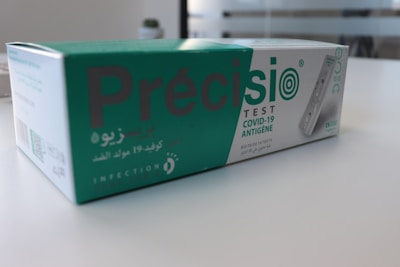 A box containing a COVID-19 antigen test kit, labeled 'Précisio Test', is placed on a white surface. The box is primarily green and white, with text in both English and Arabic. The image shows the product design and branding details.