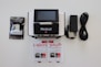 A medical device with a digital screen is centrally positioned. It is surrounded by a booklet, a package of medical supplies, and a power cable with an adapter. The booklet and package feature text.