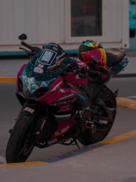 A sleek motorcycle with a vibrant, multicolored helmet resting on the seat. The bike has detailed decals and a glossy finish, parked on a concrete surface with a building in the background.