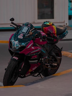 A sleek motorcycle with a vibrant, multicolored helmet resting on the seat. The bike has detailed decals and a glossy finish, parked on a concrete surface with a building in the background.