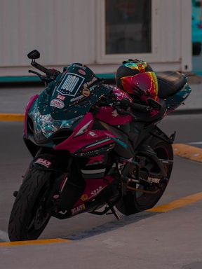 A sleek motorcycle with a vibrant, multicolored helmet resting on the seat. The bike has detailed decals and a glossy finish, parked on a concrete surface with a building in the background.