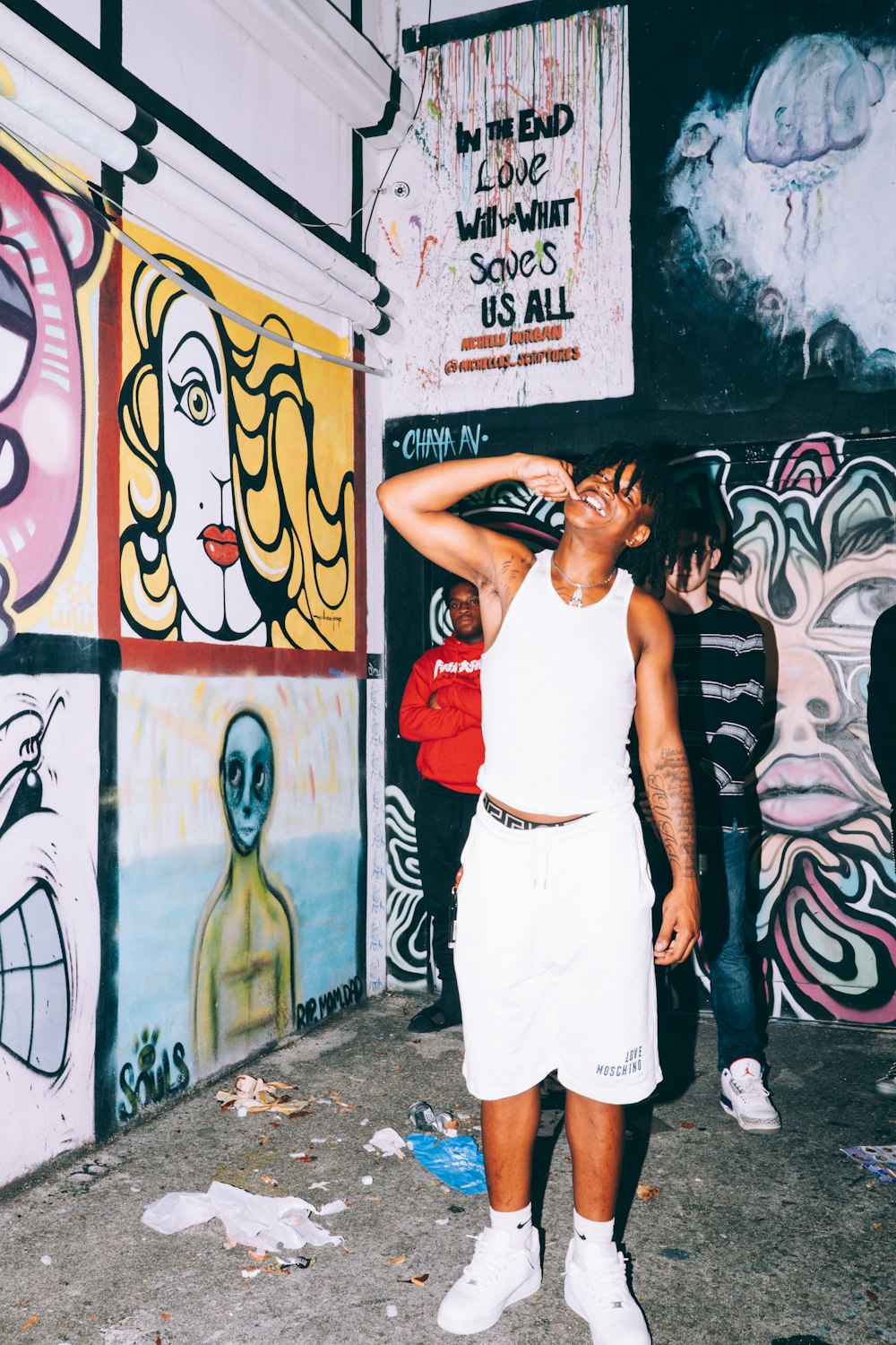 woman in white tank top and pants standing beside wall with graffiti